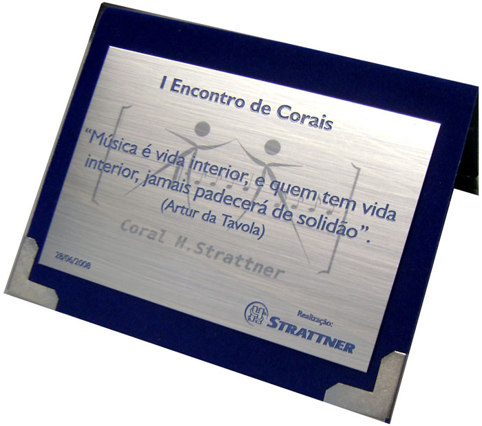 Placa de homenagem relembrando Encontro de Corais com marca d'água espelhada.